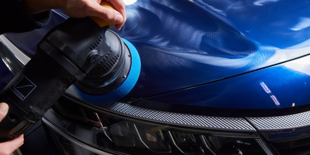 Man with an orbital polisher in car workshop polishing car closeup